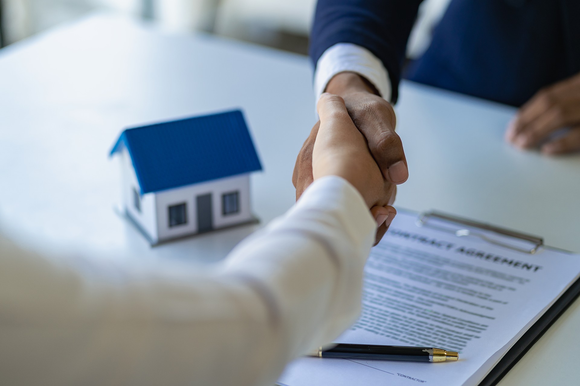 Real estate agent and client handshake after completion contract after home insurance to start project contract in office center at construction site behind model house, home loan contract concept